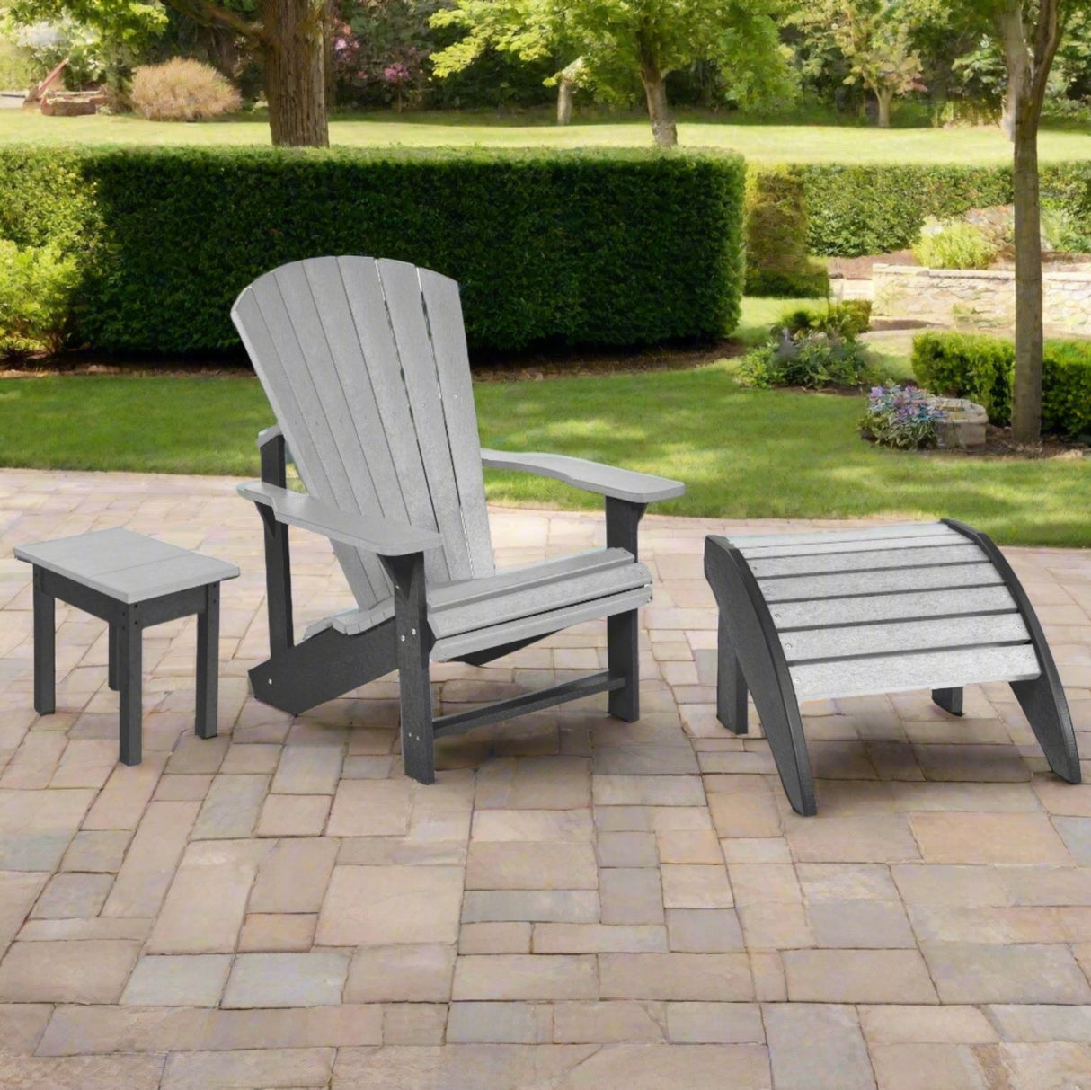 A resin patio set consisting of a small end table, an Adirondack chair and a footstool on a stone patio in a sunny backyard