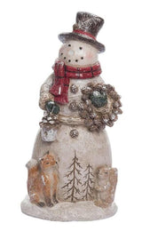 This snowman is wearing a black top hat, a red and black scarf and is holding a pine cone wreath and a bird house. There are two bare trees etched into the base of the snowman while a smiling fox and a smiling rabbit stand nearby.