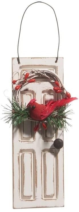 Ornament shaped like a white door. On the door is a wreath with pine needles and a cardinal accent.