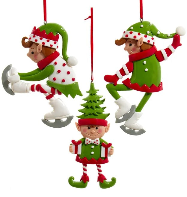 Elf ornament. There are three options. One elf is wearing a white and red polka dot jumper and ice skates. One elf is wearing a hat shaped like a tree and is holding two gifts. One elf is wearing a green jumper and wearing ice skates.