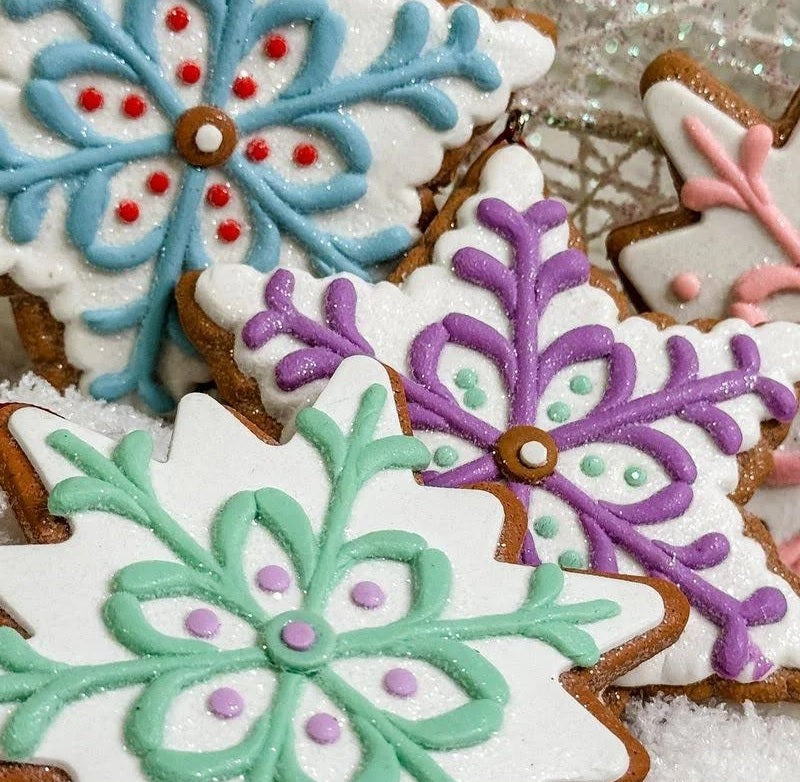 Ornament designed to look like a frosted gingerbread cookie. Two are shaped like six-point stars and two are shaped like snowflakes. They're all decorated with intricate designs. You get one, this image shows all four options.
