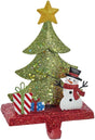 Stocking hanger covered in glitter. Designed to look like a light green tree with a yellow star on top. Next to the tree are two presents and a snowman wearing a top hat and a red scarf. The base of the holder is covered in red glitter.