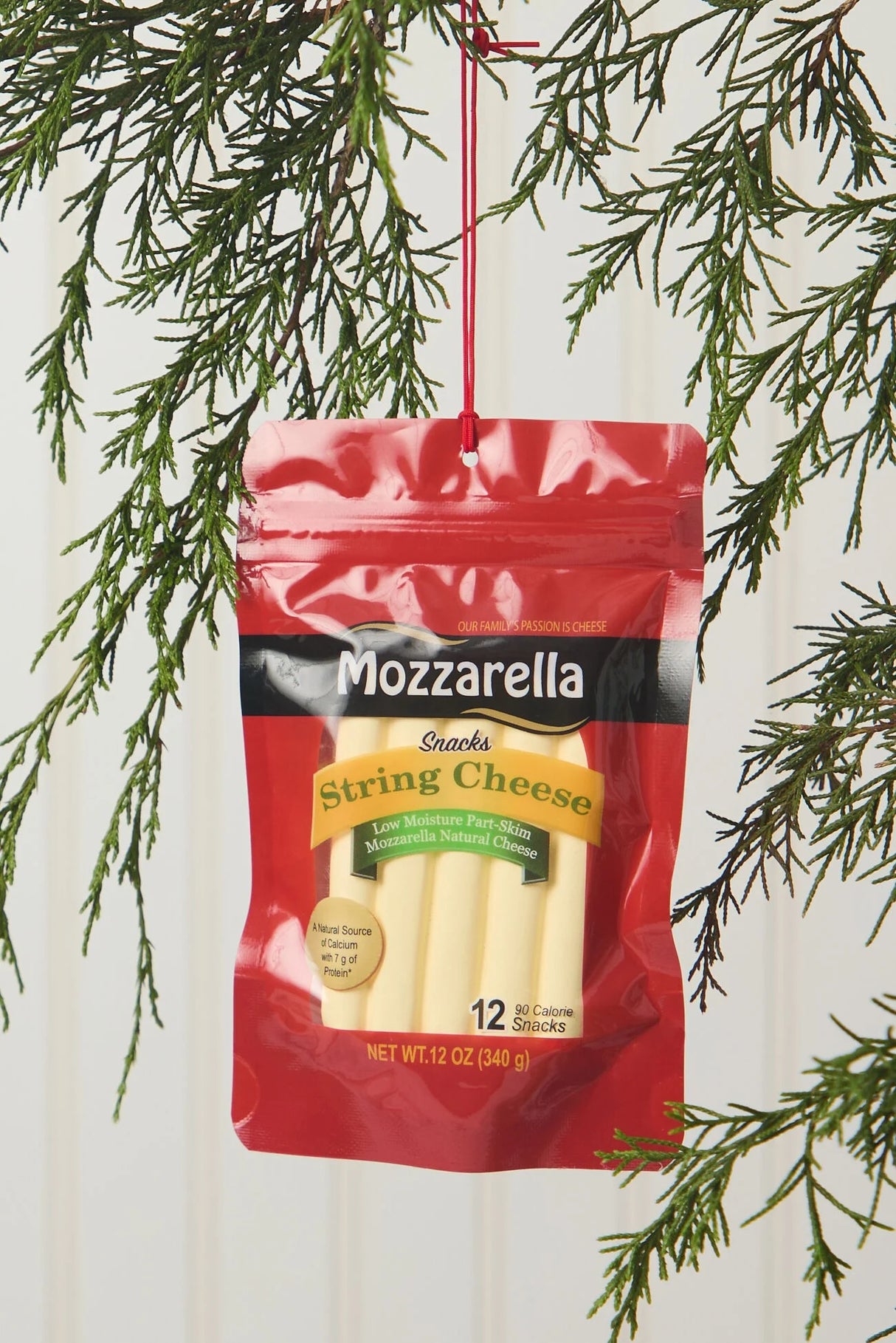 An ornament shaped like a package filled with string cheese. It reads "Mozzarella. String cheese snacks. Low moisture part-skim mozzarella natural cheese. A natural source of calcium with 7 g of Protein. 12 90 calorie snacks."
