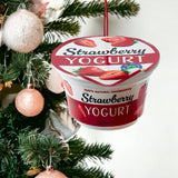 Ornament shaped like a cup of yogurt. One ornament is white and red and "flavored" strawberry. One ornament is white and blue and "flavored" blueberry. One ornament is white and orange and "flavored" peach. One ornament is white and blue and "flavored" Greek-style.