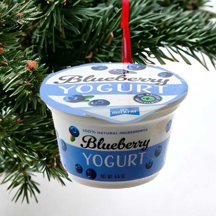 Ornament shaped like a cup of yogurt. One ornament is white and red and "flavored" strawberry. One ornament is white and blue and "flavored" blueberry. One ornament is white and orange and "flavored" peach. One ornament is white and blue and "flavored" Greek-style.