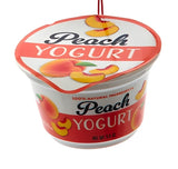 Ornament shaped like a cup of yogurt. One ornament is white and red and "flavored" strawberry. One ornament is white and blue and "flavored" blueberry. One ornament is white and orange and "flavored" peach. One ornament is white and blue and "flavored" Greek-style.
