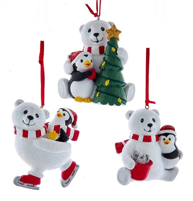 One ornament features a polar bear and a penguin decorating a Christmas tree. One ornament features a polar bear ice skating with a penguin on its back. One ornament features a polar bear and a penguin smiling over a red bucket of fish. Each ornament hangs from a red ribbon.