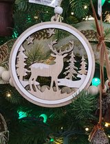Round wooden ornament with a winter scene inside. One ornament features the silhouette of a reindeer standing in the middle of a snowy forest. One ornament features different types of snowflakes and the silhouette of a reindeer among some trees and it reads "Merry Christmas."