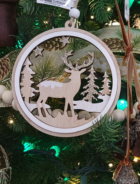Round wooden ornament with a winter scene inside. One ornament features the silhouette of a reindeer standing in the middle of a snowy forest. One ornament features different types of snowflakes and the silhouette of a reindeer among some trees and it reads "Merry Christmas."