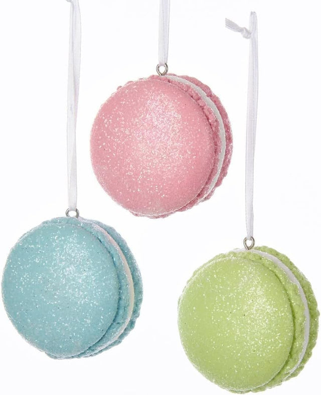 Ornaments shaped like a macaron cookie. One is pink, one is blue and one is green. They're all decorated with glitter to appear covered in sugar.