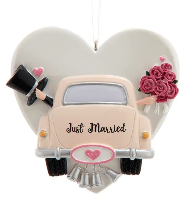 Ornament shaped like a heart with a car in front of it. Also features a top hat, delicate flowers and tin cans trailing behind. Can be personalized.