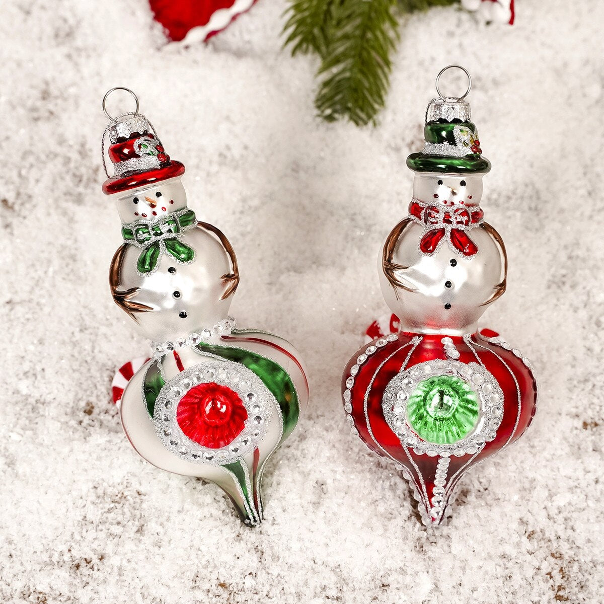 Snowman-shaped ornament. One snowman is wearing a red top hat and a green scarf. One snowman is wearing a green top hat and a red scarf. Both ornaments feature a striped design on the bottom half.