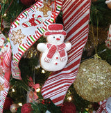 Christmas ornament designed to look like a gingerbread cookie shaped like a snowman. One snowman is wearing a green top hat and a green scarf. One snowman is wearing a red top hat and a red scarf.