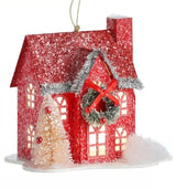 Ornament shaped like a house covered in snow. One house is red and features a wreath near the roof with a red bow. One house is green and features a wreath near the roof with a green bow.
