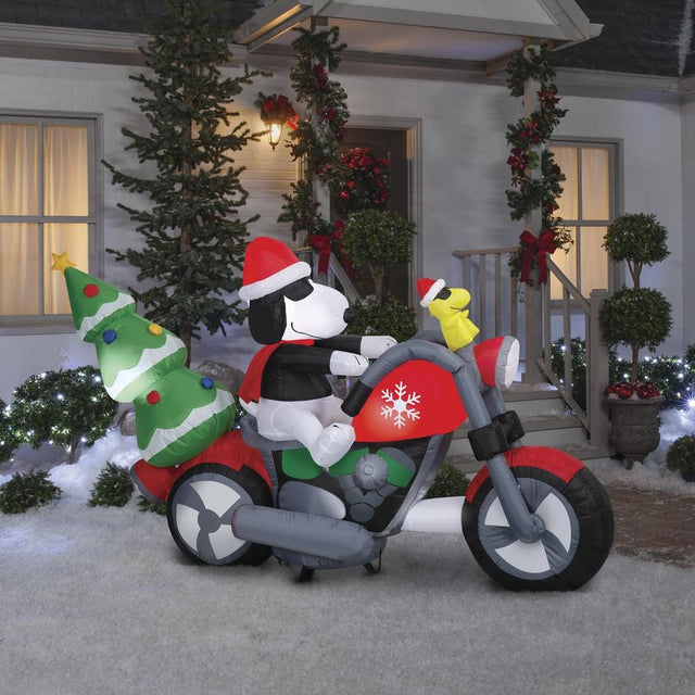 Christmas inflatable. It features Snoopy wearing a Santa hat and wearing sunglasses. Snoopy is driving a red motorcycle with a snowflake accent on it. There's a decorated Christmas tree on the back and Woodstock is riding on the handlebars. There are LED lights inside.
