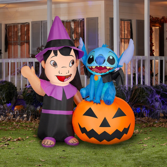 Halloween inflatable shaped like the Disney characters Lilo and Stitch dressed for Halloween. Lilo is wearing a witch costume and Stitch is wearing a collar with bat wings on it. Stitch is sitting on a jack-o-lantern.