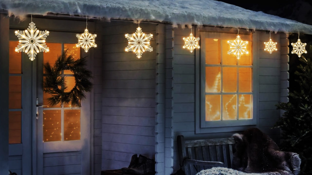 A string of warm white twinkling snowflake icicle lights hanging off the snowy roof of a house.