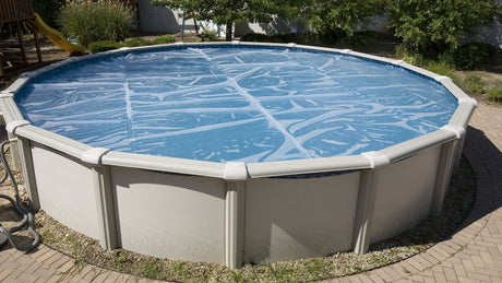 This is a lifestyle image showing the oval shaped clear solar cover on top of an oval shaped pool.