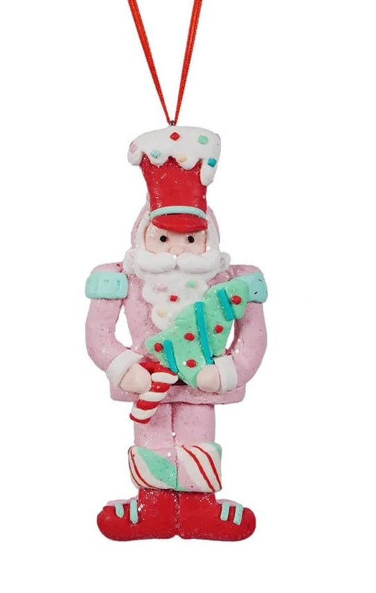 This ornament features a toy soldier wearing a pink outfit, a red hat and he's holding a small tree with a peppermint trunk.