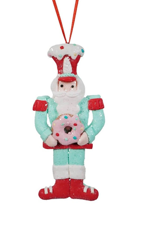 This ornament features a toy soldier wearing a light blue outfit, a red hat and he's holding a pink donut.