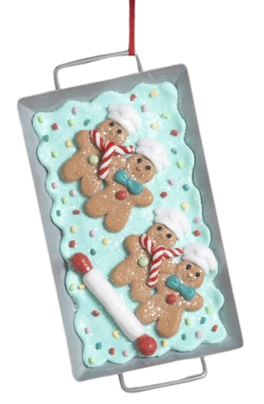 This image shows an ornament that features gingerbread men on a blue frosting base next to a rolling pin.