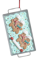 This image shows an ornament that features gingerbread men on a blue frosting base next to a rolling pin.