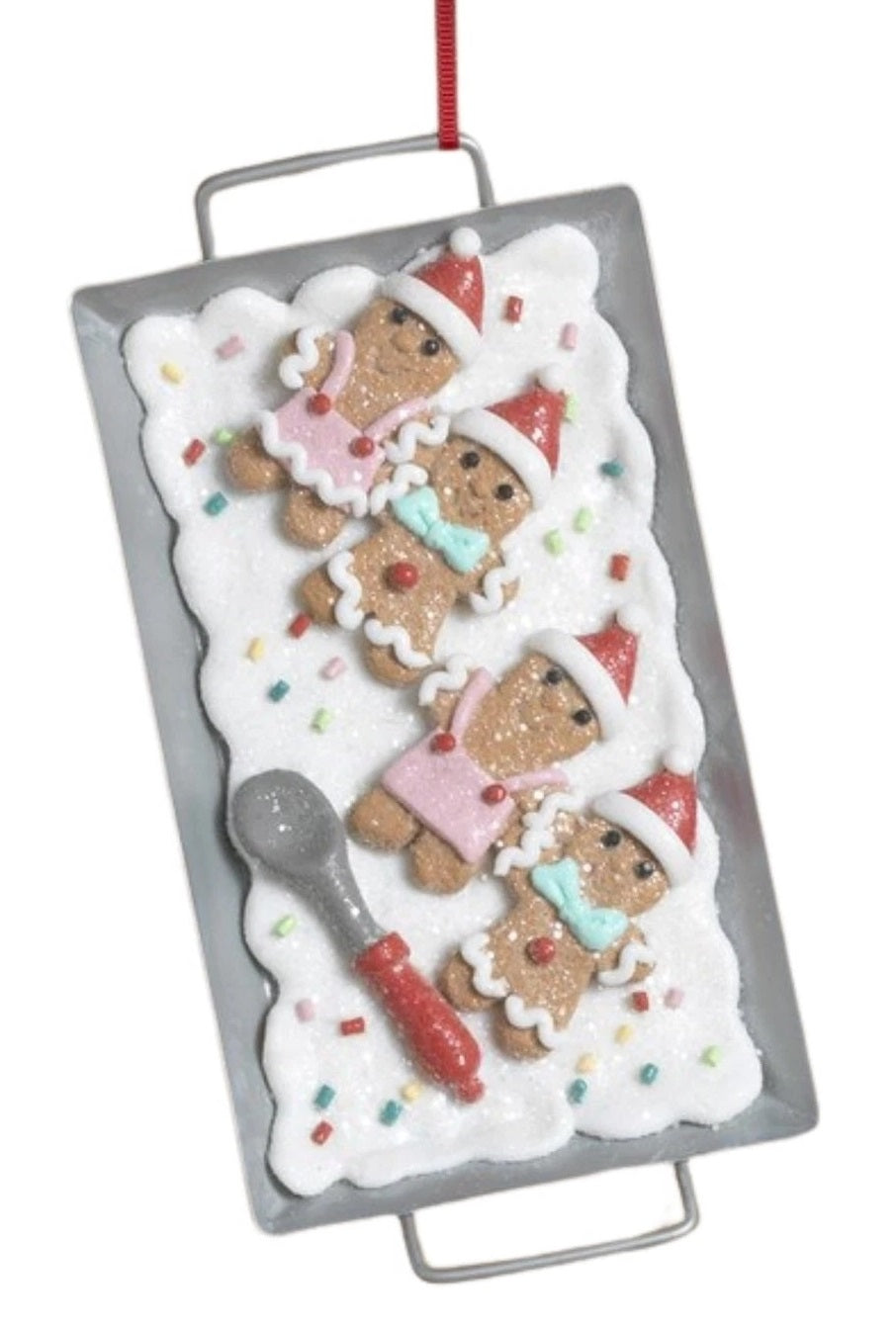 This image shows the ornament that features gingerbread men on a white frosting base next to a spoon.