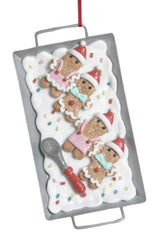 This image shows the ornament that features gingerbread men on a white frosting base next to a spoon.