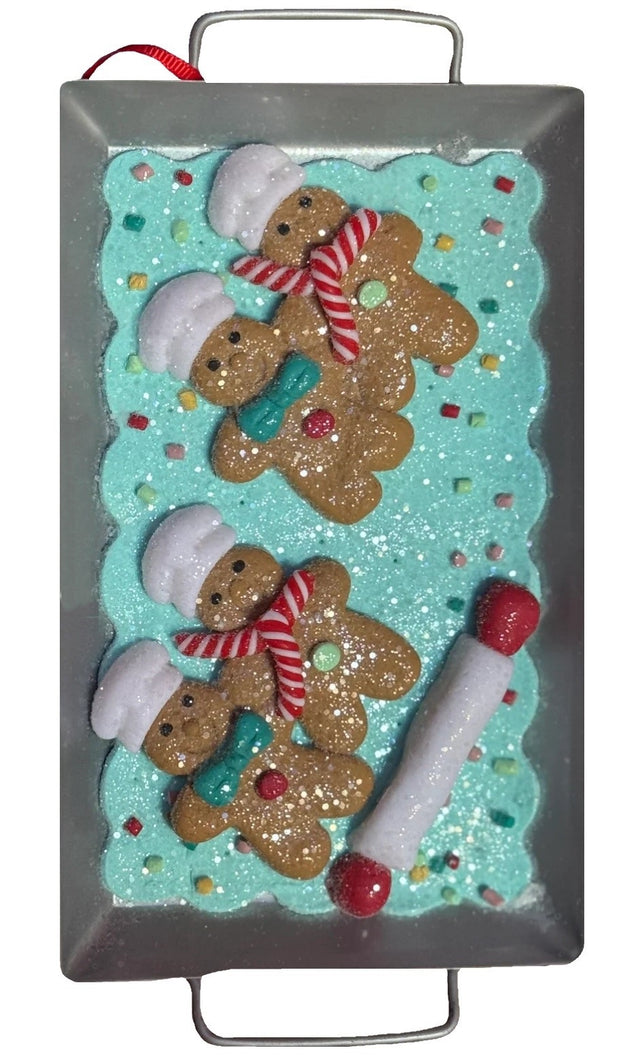 This image shows an ornament that features gingerbread men on a blue frosting base next to a rolling pin.