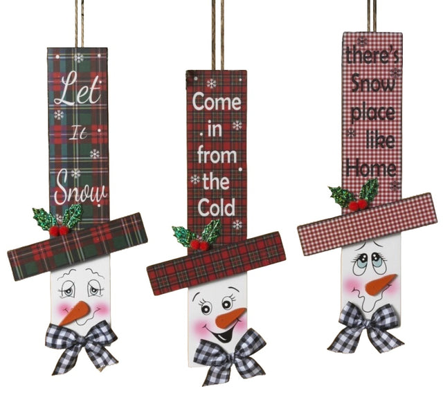 Hanging sign designed to look like a snowman head. One snowman has a red and green buffalo check top hat that reads "Let It Snow." One snowman has a red and green plaid top hat that reads "Come in from the Cold." One snowman has a red and white plaid top hat that reads "There's Snow place like Home."
