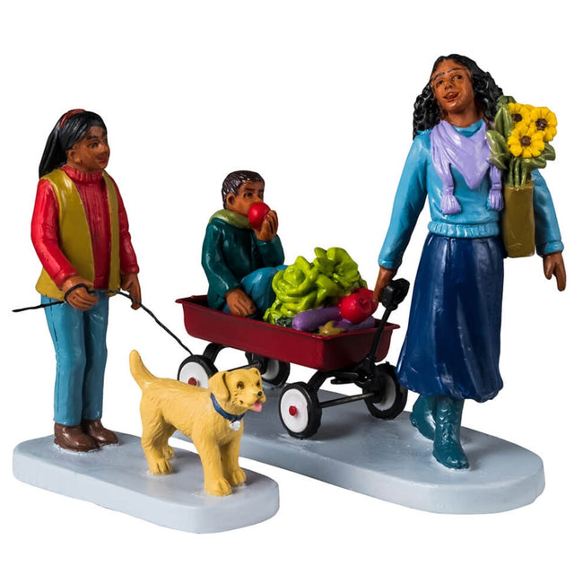Resin figurines for a Lemax Village display. Designed to look like a mom and her two children. The mom is pulling a red wagon with a boy eating an apple in it. The mom is also holding a bag of sunflowers. The young girl is walking her dog on a leash. They're all wearing winter-y type clothes.