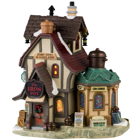 Porcelain lighted building for a Lemax display. Designed to look like an old-timey building with a circular sun room off to the side. The windows are multi-colored stained glass. There are signs advertising stews, soups, goulash, Brunswick stew, clam chowder, chicken noodle soup, vegetables and potatoes. There's also a sign that reads "New Holiday Menu and Later Hours!" There's snow on the roof and the sidewalk.