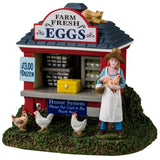 Resin table accent for a Lemax display. Designed to look like a red booth on a grassy patch. There's a sign on the roof that reads "Farm Fresh Eggs. $3.00 a Dozen." There's a cat lounging on the roof and three chickens standing on the ground. The booth is filled with shelves of eggs with a yellow box on the counter. Another sign reads "Honor System. Please put cash in box, thank you." A young girl stands near the booth holding a chicken and a basket of eggs. She's wearing a floppy hat and a white apron.