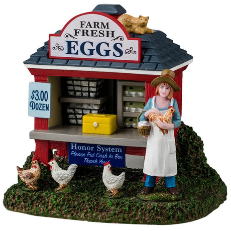 Resin table accent for a Lemax display. Designed to look like a red booth on a grassy patch. There's a sign on the roof that reads "Farm Fresh Eggs. $3.00 a Dozen." There's a cat lounging on the roof and three chickens standing on the ground. The booth is filled with shelves of eggs with a yellow box on the counter. Another sign reads "Honor System. Please put cash in box, thank you." A young girl stands near the booth holding a chicken and a basket of eggs. She's wearing a floppy hat and a white apron.