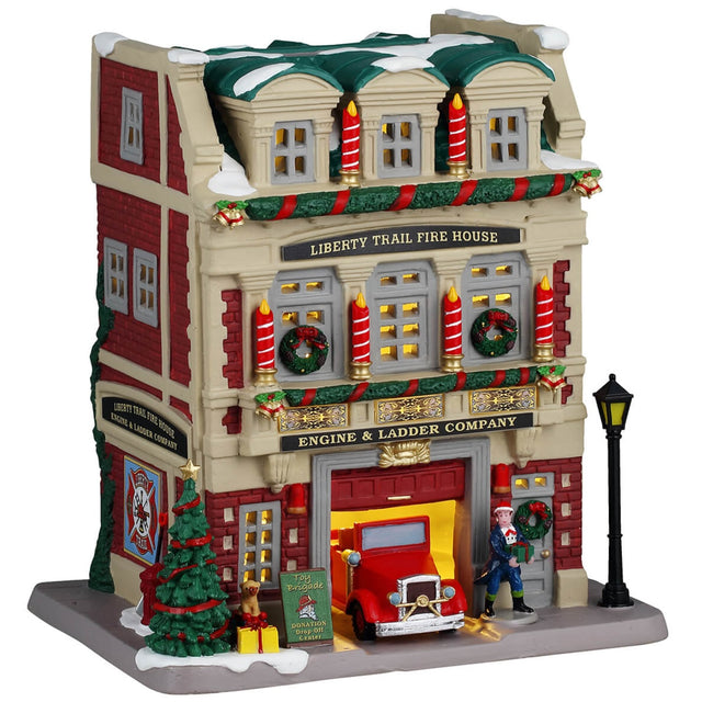 Porcelain lighted building for a Lemax display. Designed to look like a red brick fire house. There are large red and white striped candle accents, decorated wreaths and a Christmas tree. You can see the red firetruck in the garage and there's a lamppost next to the front door. There's snow on the roof and on the sidewalk.