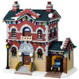 Porcelain lighted building for a Lemax display. Designed to look like a red, yellow and gray brick police precinct office. The roof and sidewalk has snow on it. There are multi-colored lights hanging from the roof. The windows have wreaths and there's a car coming out of the side garage. 