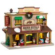 Porcelain lighted building for a Lemax display. Designed to look like a Western building. On top of the building, it says "Est. 1886." There's a large wreath near the roof and a picture of a buffalo. There's snow on the roof and a bunch of Christmas accents throughout. Accents include: a decorated Christmas tree, a Santa bag with presents and a candy cane inside, there are presents and a snowman wearing a cowboy hat.