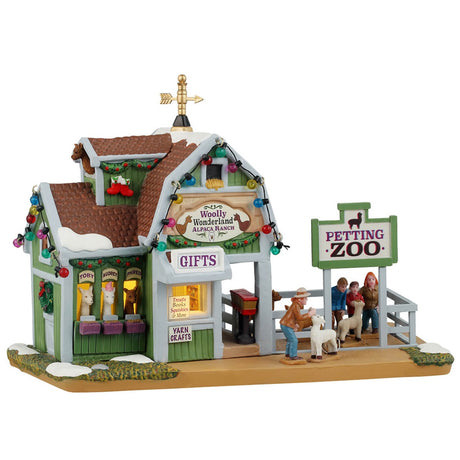 Resin lighted building for a Lemax display. Designed to look like a green barn turned into a petting zoo. There's a gold wind vine on the roof and multi-colored lights hanging on the roof. There are alpacas looking out the windows. Their names are Toby, Audrey and Phred. There are signs that read "Gifts," "Treats, Books, Squishes & More" and "Yarn Crafts." There are people feeding small goats behind a gray fence.