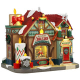 Resin lighted building for a Lemax display. Designed to look like a candle shop covered in snow. There are candle accents and wreaths and garland. There's a dog peering into the window to watch Kristin make candles.