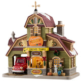 Porcelain lighted building for a Lemax display. Designed to look like a house turned into a drive-thru restaurant. There's a gold wind vine and snow on the roof. There are fall accents as well as wreaths and pine swag decorations. There's a red car ordering food in the drive thru. There's a boy sitting on a bale of hay next to a white dog. You can see a woman inside the building serving coffee.
