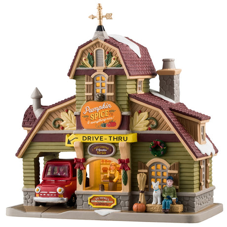 Porcelain lighted building for a Lemax display. Designed to look like a house turned into a drive-thru restaurant. There's a gold wind vine and snow on the roof. There are fall accents as well as wreaths and pine swag decorations. There's a red car ordering food in the drive thru. There's a boy sitting on a bale of hay next to a white dog. You can see a woman inside the building serving coffee.