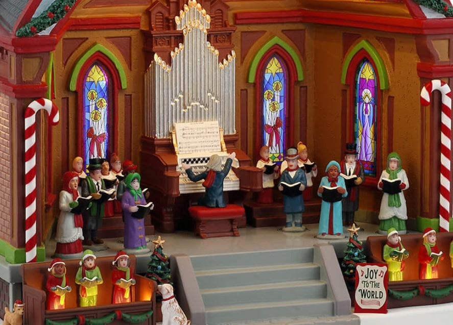 Resin lighted building for a Lemax display. Designed to look like a choir performing at a pavilion. There's a large organ, kids dressed like elves, two dogs, two peppermint candy cane accents, a decorated garland on the roof and a sign that reads "Joy to the World." The ceiling of the pavilion is decorated with different colored poinsettias.