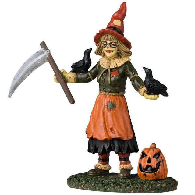 Resin figurine for a Lemax display. Designed to look like a female scarecrow. She has a scythe, a pointy red witch hat, glasses and there are two crows sitting on her arms. There's a carved jack-o-lantern next to her in the grass.
