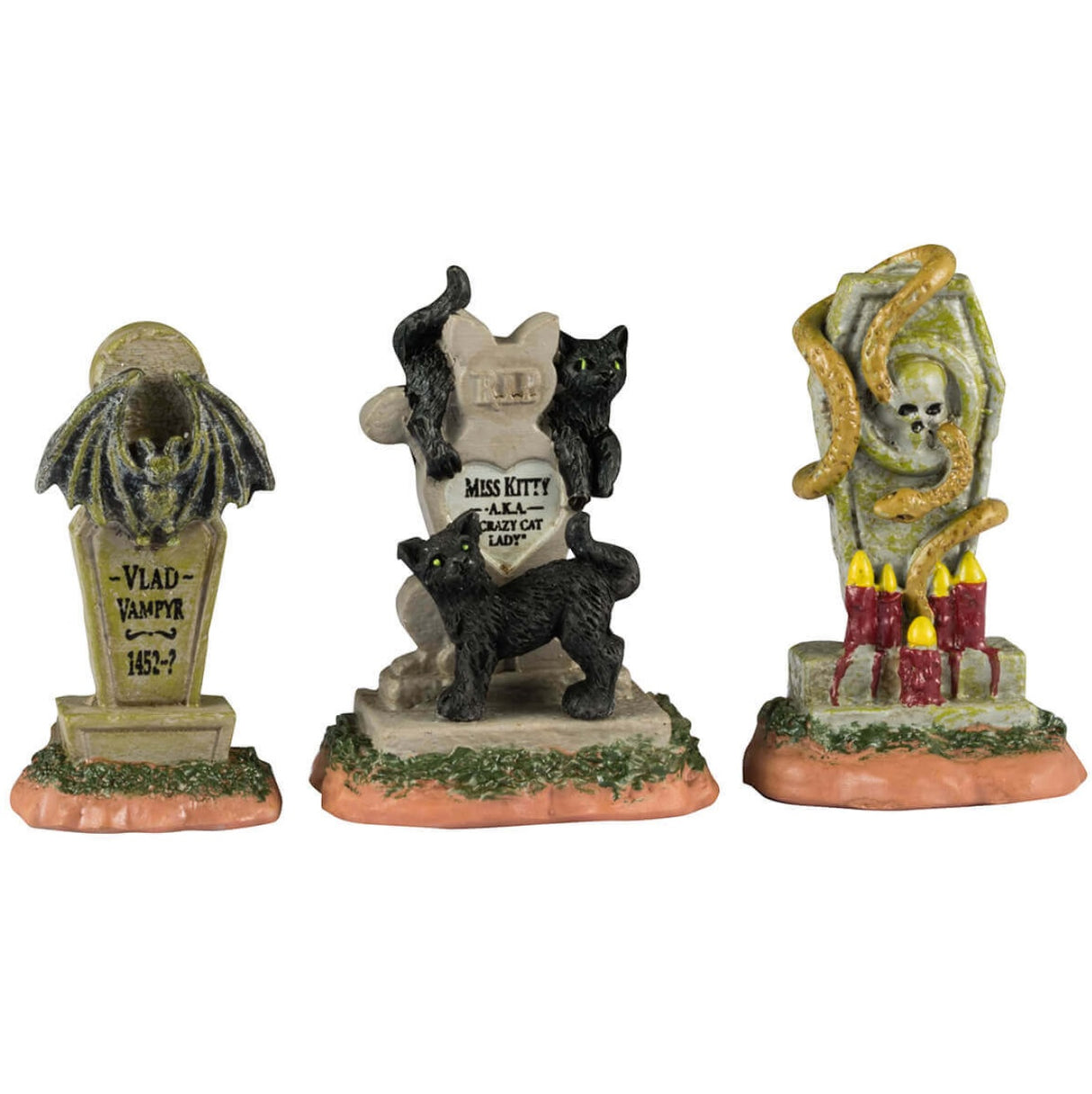 Resin village accents for a Lemax display. Designed to look like three headstones. One has a bat statue on it and it reads "Vlad Vampyr 1452-?" The next one is shaped like a cat and reads "RIP Miss Kitty aka Crazy Cat Lady." There are black cats on it. The next one features a skull with snakes coming out of it and a bunch of red candles lit at the base.