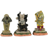 Resin village accents for a Lemax display. Designed to look like three headstones. One has a bat statue on it and it reads "Vlad Vampyr 1452-?" The next one is shaped like a cat and reads "RIP Miss Kitty aka Crazy Cat Lady." There are black cats on it. The next one features a skull with snakes coming out of it and a bunch of red candles lit at the base.