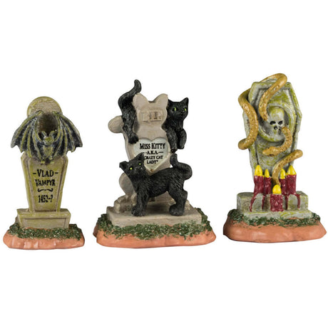 Resin village accents for a Lemax display. Designed to look like three headstones. One has a bat statue on it and it reads "Vlad Vampyr 1452-?" The next one is shaped like a cat and reads "RIP Miss Kitty aka Crazy Cat Lady." There are black cats on it. The next one features a skull with snakes coming out of it and a bunch of red candles lit at the base.