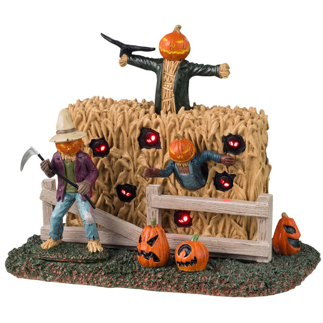Plastic village accent for a Lemax Spooky Town display. Designed to look like three scarecrows with jack-o-lantern heads coming out of a cornfield. There are glowing red eyes and pumpkins.