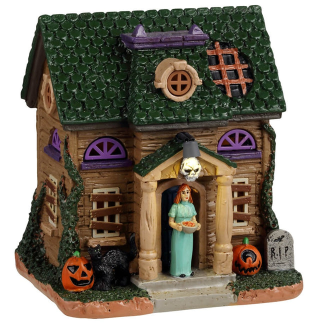 Resin building for a Lemax display. Designed to look like a rundown house. Part of the roof is missing and the windows are boarded up. There's a woman wearing a light blue dress in the doorway handing out candy. There's a black cat and two carved pumpkins and a tombstone that reads RIP.
