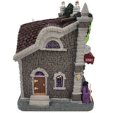 Resin lighted building for a Lemax display. Designed to look like a gothic wig store. The sign reads "WICKED WIGS" and looks like the top of Frankenstein's head. There's also a statue of the Bride of Frankenstein. There are skulls and pumpkins and cousin IT standing outside. They sell zombie wigs, vampire wigs, clown wigs and more.