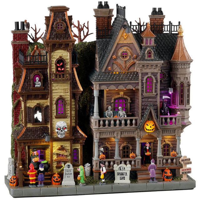 Resin lighted building for a Lemax display. Designed to look like a two Victorian-era style mansions standing next to each other. The one on the left is run down with boarded windows. The one on the right looks bright and regal. There are kids trick or treating at both homes and monsters, skeletons and ghosts in the windows.